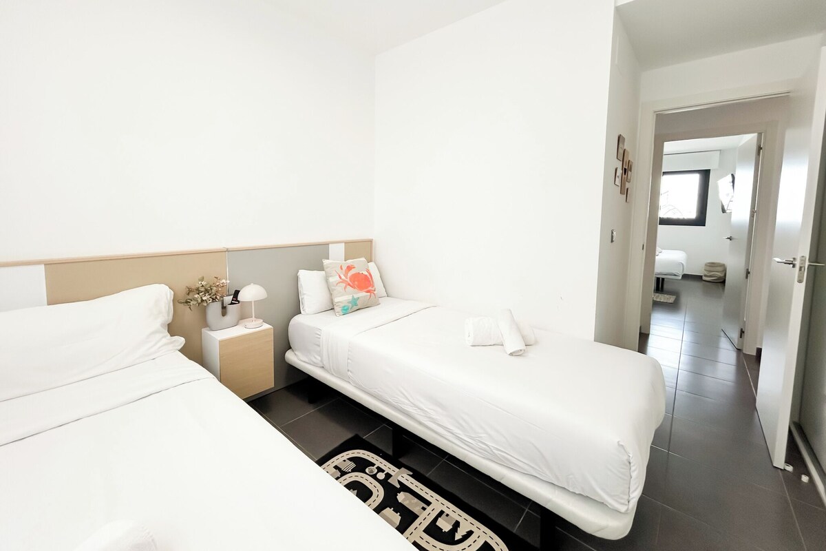 A modern hotel room with two beds, a nightstand with a lamp, and a decorative rug.