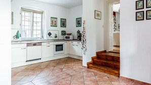 A kitchen with white cabinets, a microwave, and a coffee maker. There are framed pictures on the wall and a staircase leading to another room.