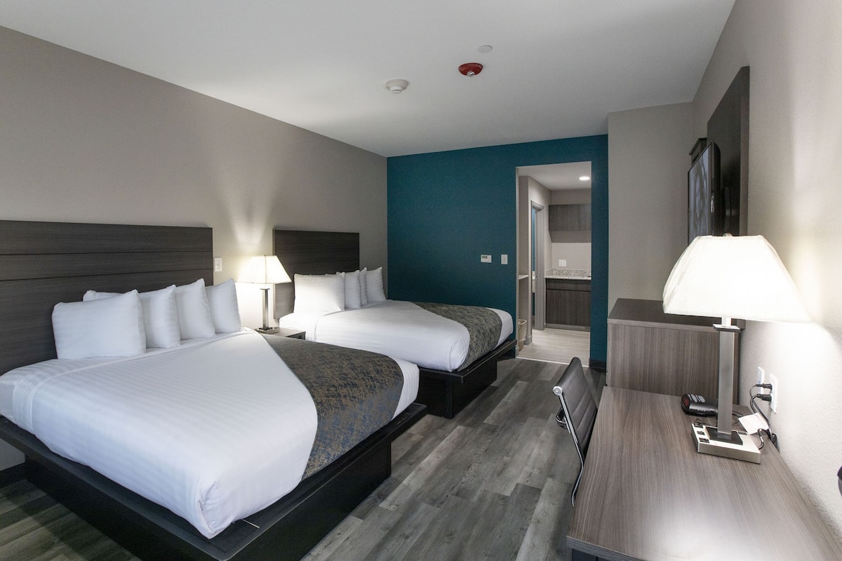 A hotel room with two beds, a desk, a chair, a lamp, and a mirror.