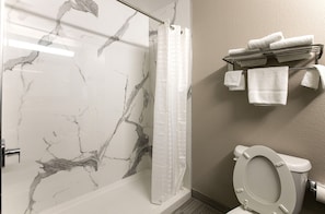 Un baño con pared de mármol, cortina de ducha, inodoro y toallero con toallas.