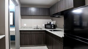 A compact kitchen with dark wood cabinets, a stainless steel sink, a microwave, and a black refrigerator.