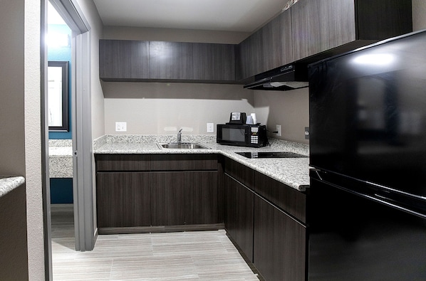 Una cocina compacta con armarios de madera oscura, un lavamanos de acero inoxidable, un microondas y un refrigerador negro.