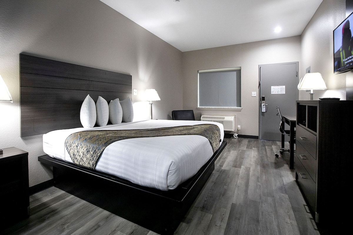 A modern hotel room with a large bed, bedside lamps, a dresser, and a television on the wall.