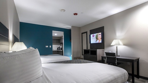 A hotel room with a bed, a desk, a TV, and a bathroom visible through an open door.