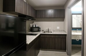 Una cocina compacta con armarios de madera oscura, un lavamanos de acero inoxidable y un refrigerador negro.