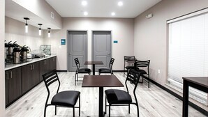 A modern kitchen with dark cabinets, a coffee station, and a dining area with a table and chairs.