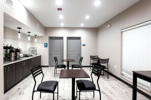 A modern kitchen with dark cabinets, a coffee station, and a dining area with a table and chairs. - Express Inn (Rosenberg)