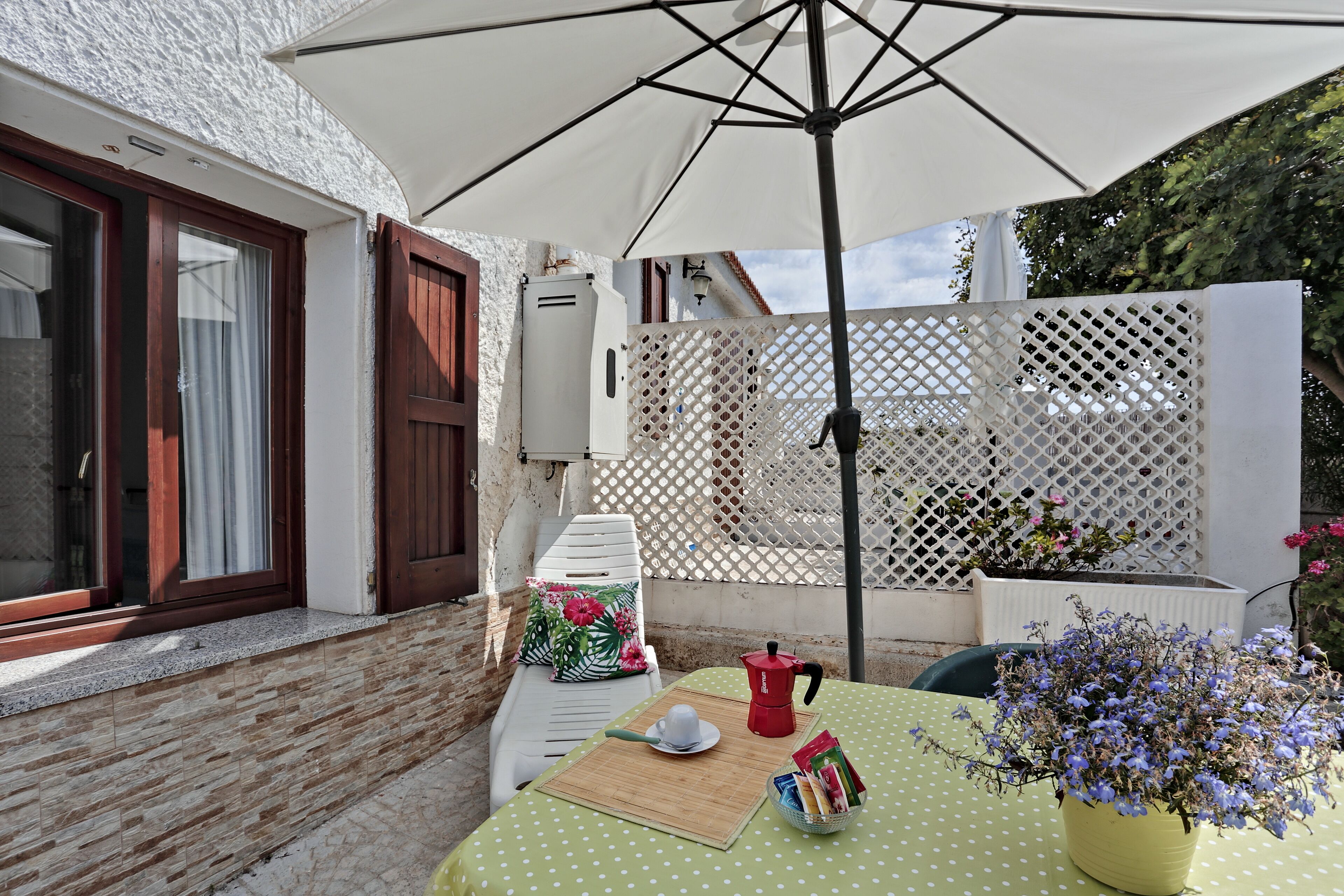A patio with a table set for two, a white umbrella, and a potted plant.
