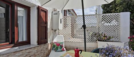 A patio with a table set for two, a white umbrella, and a potted plant.