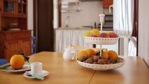 A dining table with a white teapot, a cup, a bowl of fruit, and a plate with an orange. - Il Melo Residence (Porto Torres)