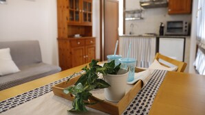 A dining table with a tray holding a potted plant and two cups, a wooden cabinet, a kitchen area with a microwave and toaster, and a grey sofa in the background. - Il Melo Residence (Porto Torres)