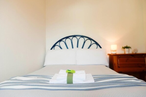 A neatly made bed with a striped bedspread and pillows, a wooden nightstand with a lamp and a small plant, and a metal headboard. - Il Melo Residence (Porto Torres)