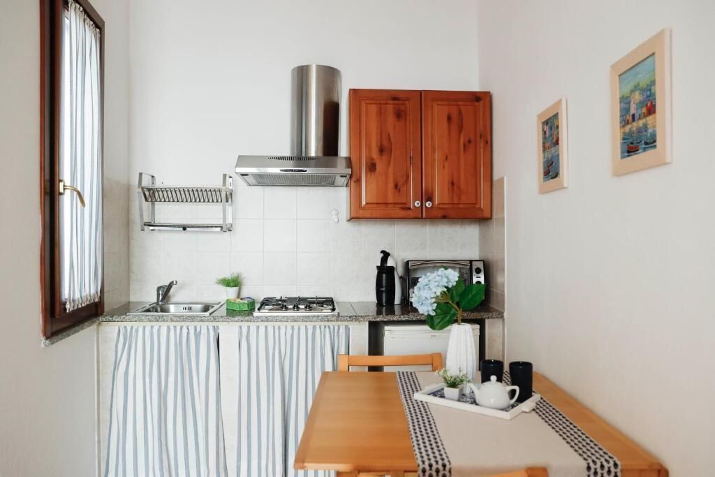 Een compacte keuken met een gasfornuis, een rvs afzuigkap, houten kastjes en een eethoek met een geruit tafelkleed.