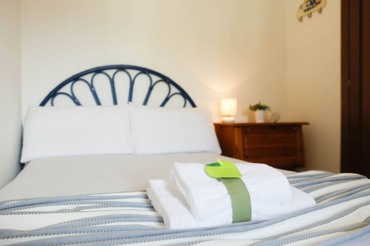 A neatly made bed with a striped bedspread and a folded white towel with a green tag on it.