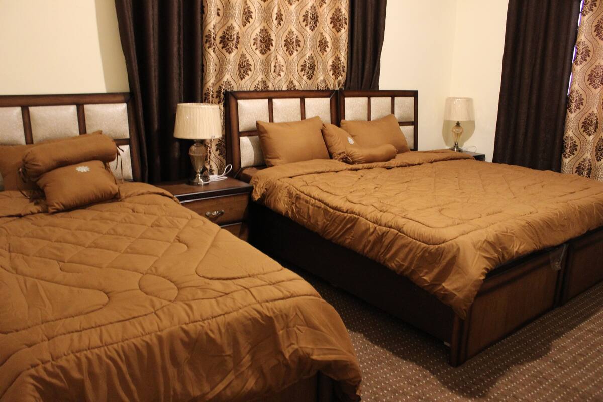 Une chambre d’hôtel avec deux lits, chacun recouvert d’une courtepointe marron matelassée et agrémenté d’oreillers assortis. On y trouve deux tables de chevet avec des lampes, ainsi qu’un panneau décoratif mural.