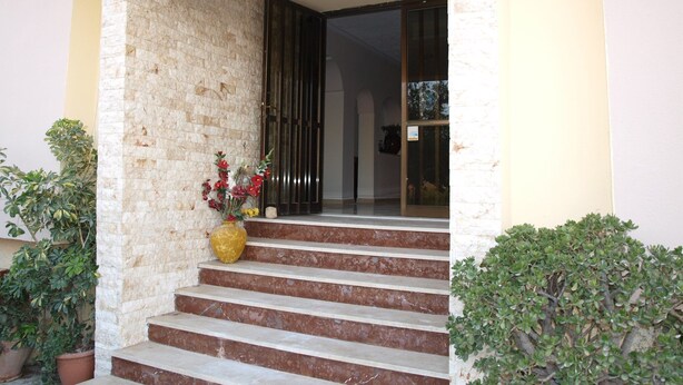A building entrance with a stone facade, a set of stairs leading to a dark door, and potted plants on either side. - Hotel Pyrgos (Chania)