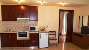 A compact kitchen with a microwave, refrigerator, and a small sink. There is a wooden cabinet above the sink and a chair next to the refrigerator. - Hotel Pyrgos (Chania)