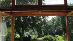 Een kamer met een groot raam dat uitzicht biedt op een tuin met een vijver, bomen en een beeld.