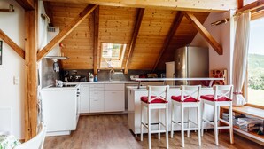 Een keuken met witte kastjes, een houten plafond en een raam met uitzicht op een groen landschap.