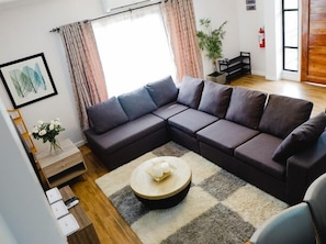 Un salon moderne avec un canapé d’angle, une table basse ronde et une plante en pot.