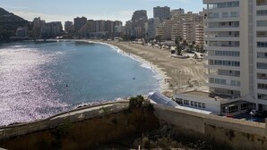 A coastal cityscape with a beach, high-rise buildings, and a prominent white building with balconies. - IFACH II 5th floor Gate 35 (Calp)