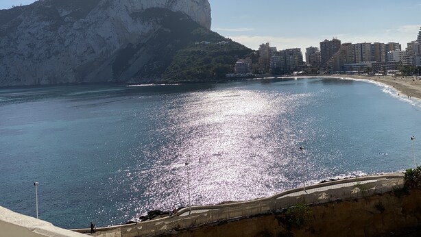 A coastal cityscape with a prominent mountain, a beach, and a promenade. - IFACH II 5th floor Gate 35 (Calp)