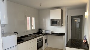 A compact kitchen with white cabinets, a microwave, a coffee maker, and a washing machine. - IFACH II 5th floor Gate 35 (Calp)