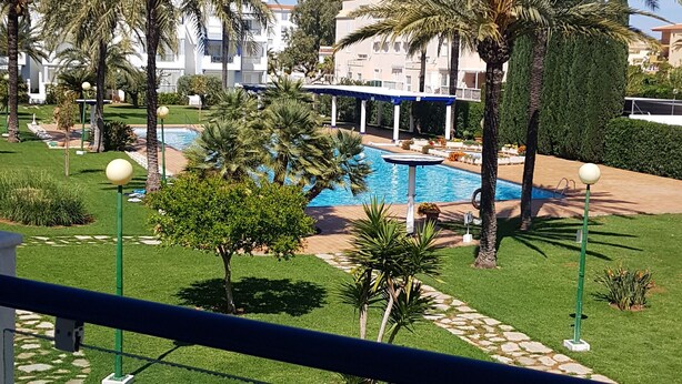 A pool area with palm trees and a building in the background. - Exclusive studio Cala Blanca (Dénia)