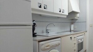 A compact kitchen with a built-in washing machine, a sink, and a stove. - Exclusive studio Cala Blanca (Dénia)