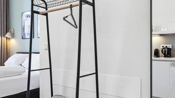 A room with a bed, a black metal drying rack, a fan, and a large mirror on the wall.