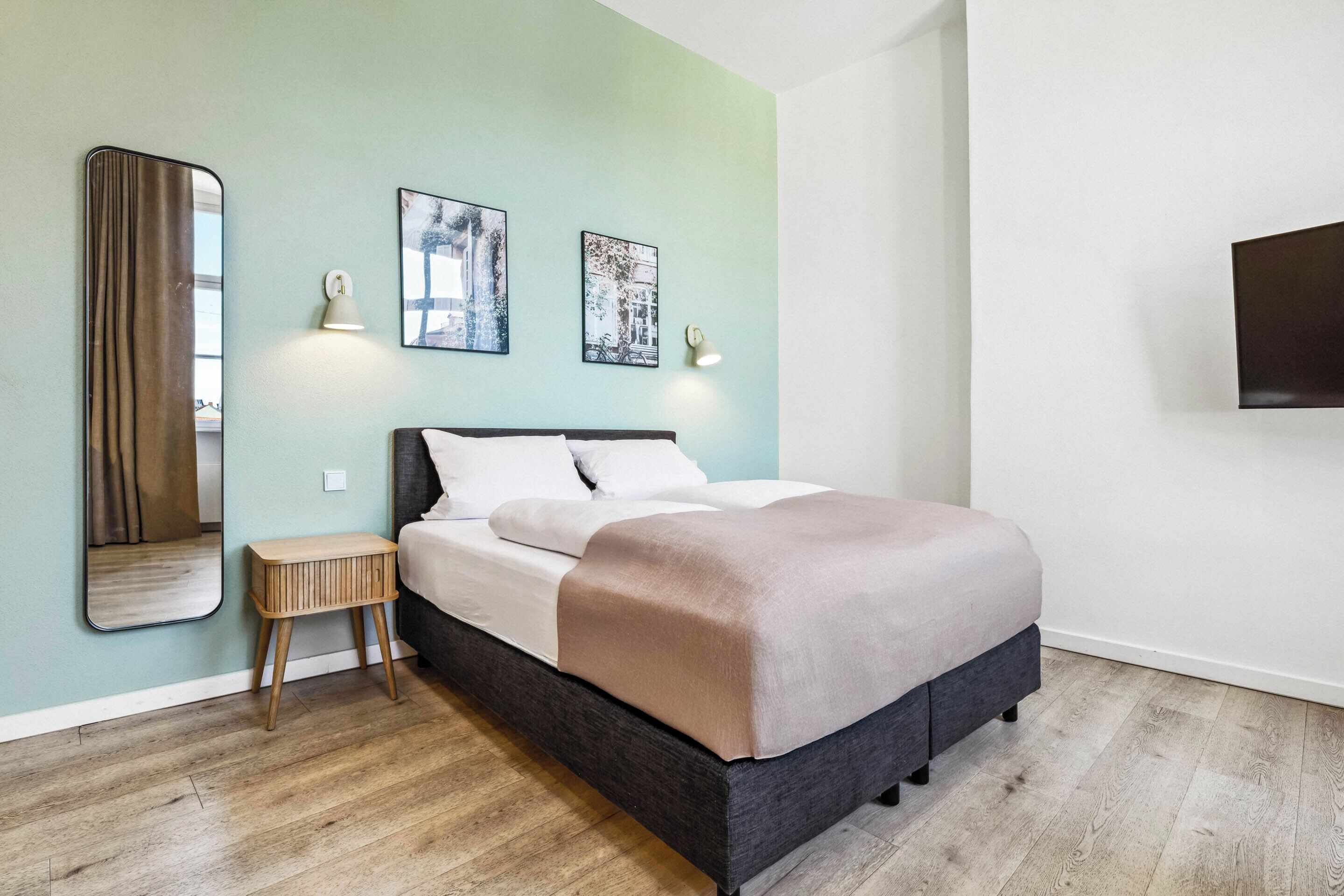 A bedroom with a bed, a bedside table, a mirror, and wall-mounted lights.