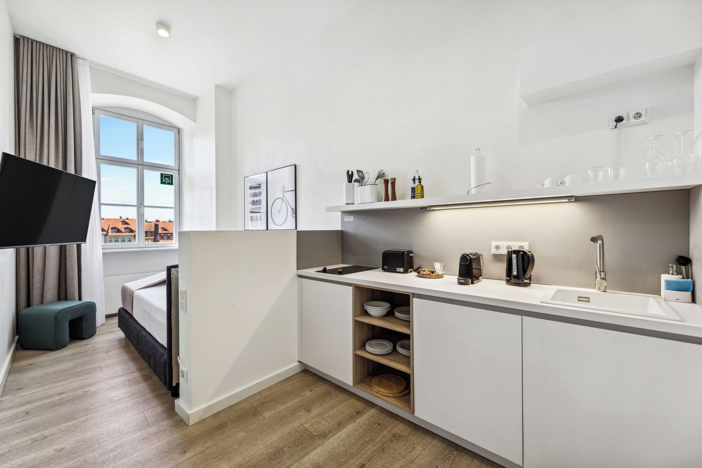 Una cucina moderna con mobili bianchi, un lavello integrato e un televisore a schermo piatto.