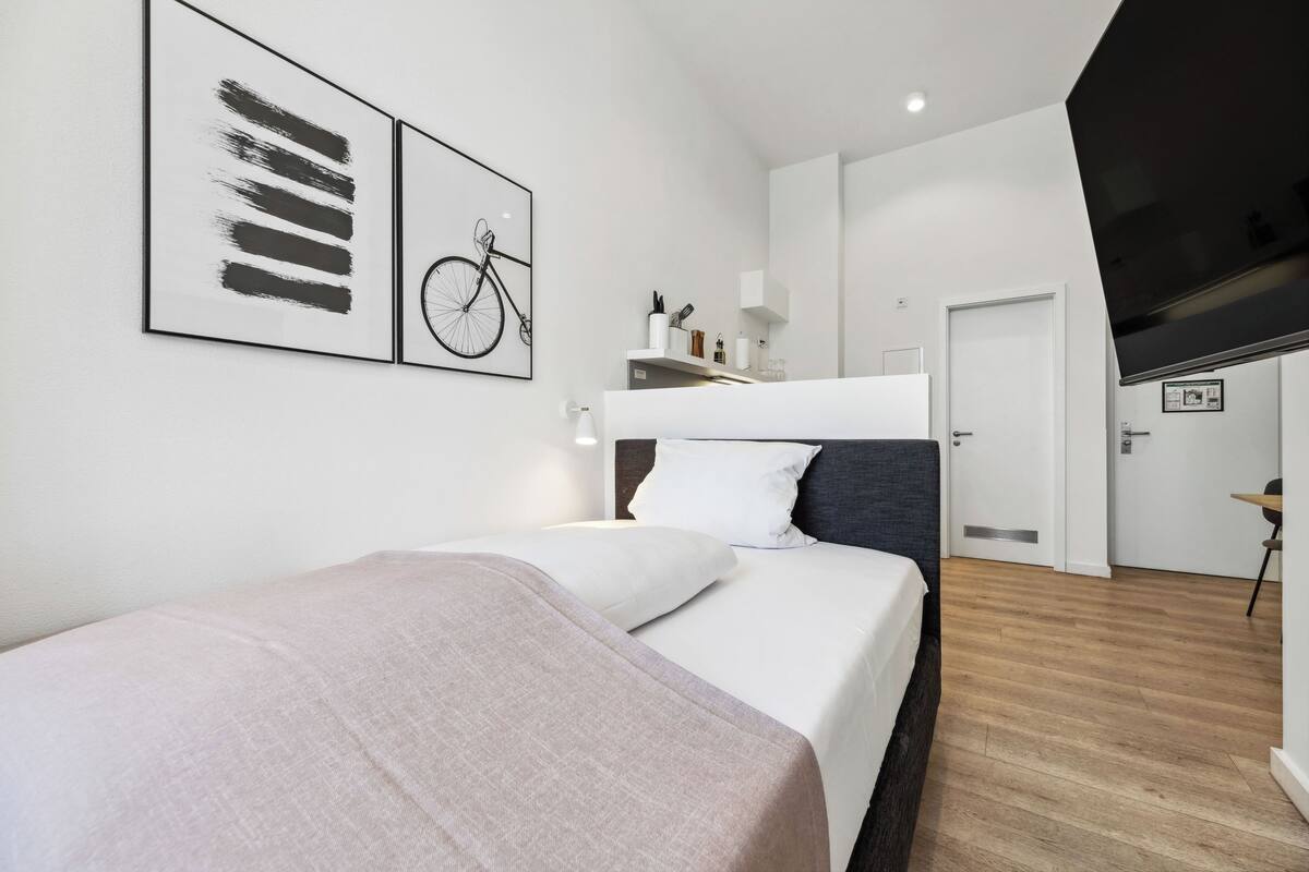 Ein modernes Hotelzimmer mit einem Bett, einem Kopfteil, einem an der Wand montierten Fernseher und einer Tür zu einem Badezimmer.