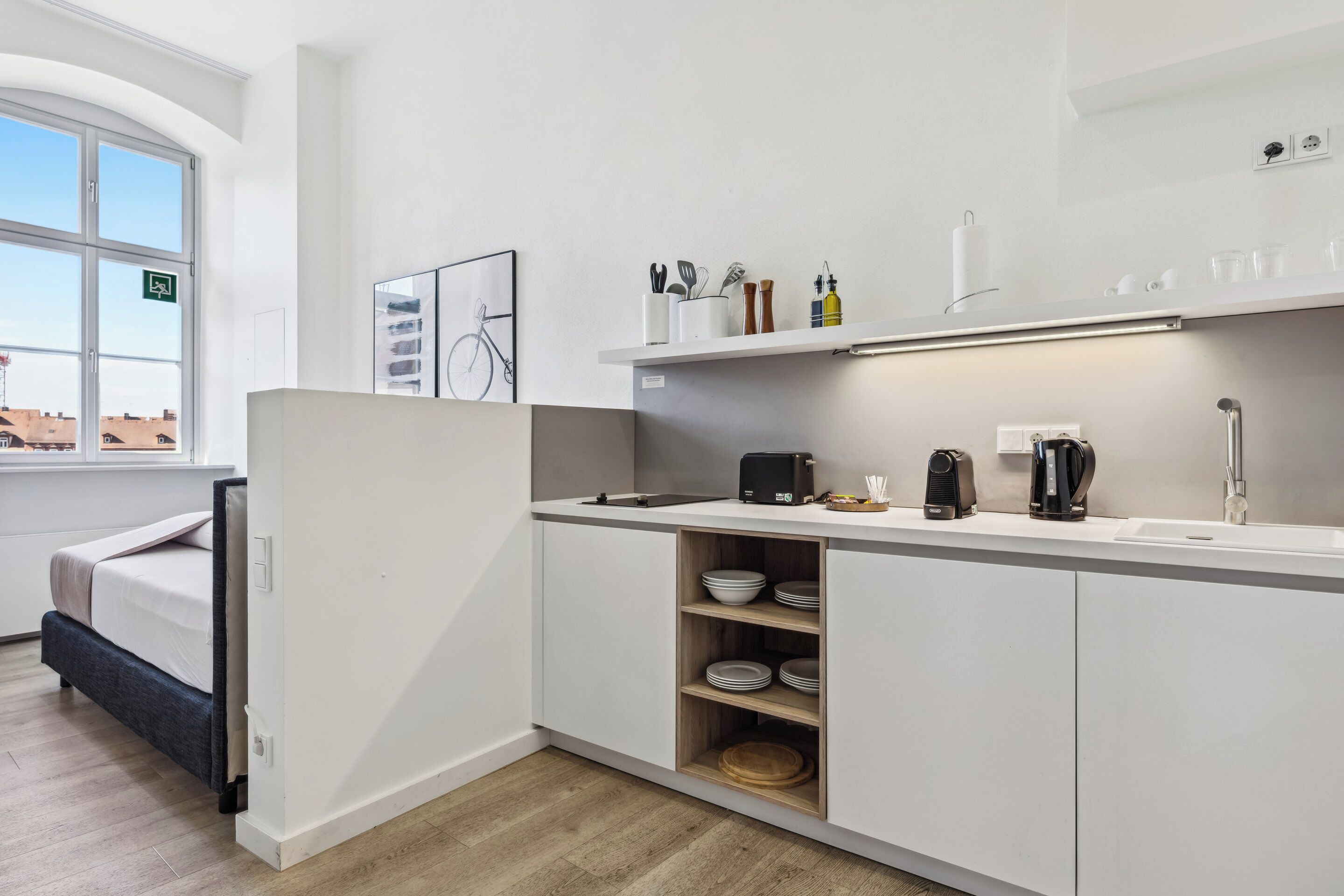 Una cocina compacta con armarios blancos, un estante empotrado con utensilios de cocina, una cafetera y vistas a la ciudad a través de un amplio ventanal.