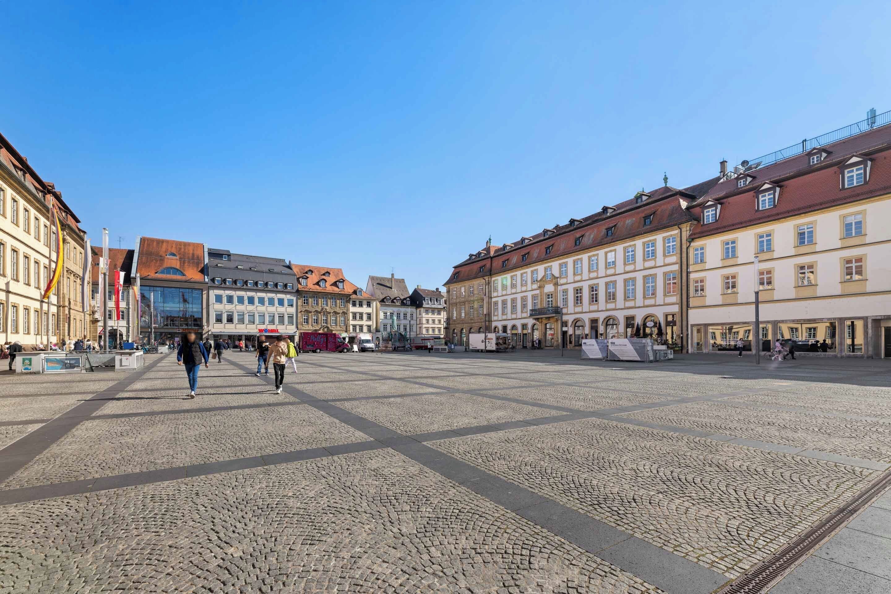A cobblestone square with historic buildings, a clear sky, and people walking.