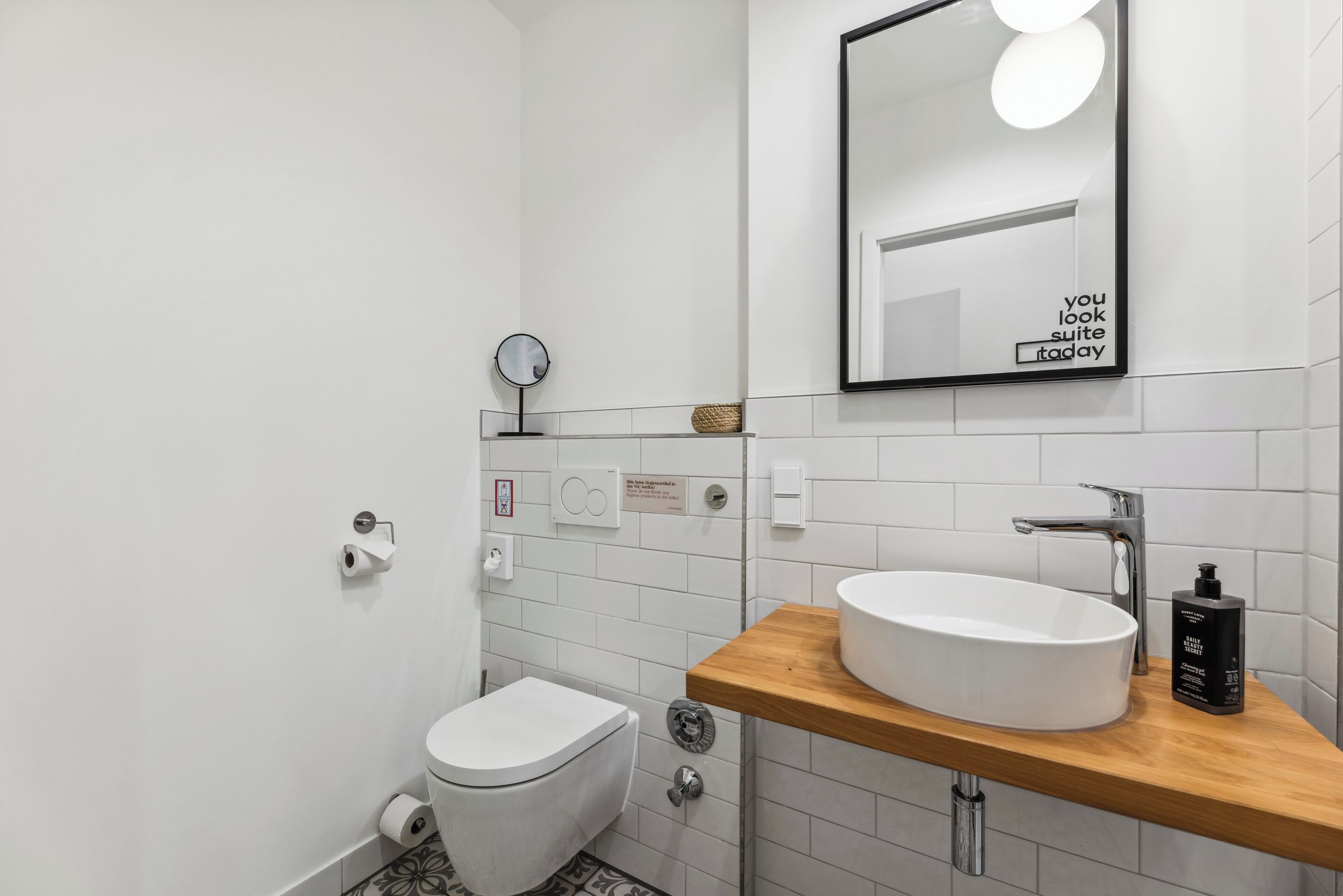 Un baño moderno con inodoro, lavamanos, espejo y un cartel sobre el espejo.