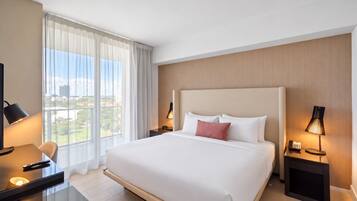 Habitación de hotel con una cama grande, un escritorio con lámpara, una silla y vista a la ciudad por la ventana.
