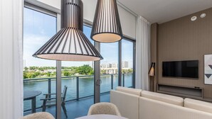 A modern hotel room with a balcony, large windows, a TV, and a dining area.