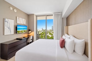 A hotel room with a large bed, a desk, a TV, and a balcony with a city view.