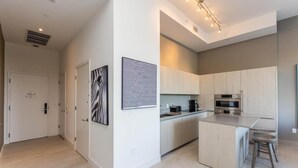 A modern kitchen with light wood cabinets, stainless steel appliances, and a small island with stools.