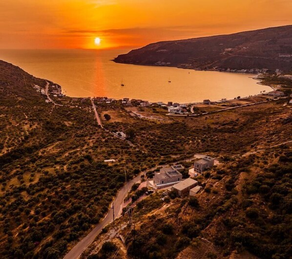 Un pueblo costero con edificios a lo largo de la orilla, una carretera que atraviesa el pueblo y un atardecer sobre el mar.