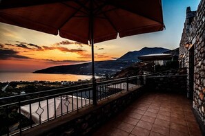A balcony with a view of a sunset over the sea and mountains.