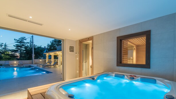 Een modern zwembad met een hottub, ligbedden en een houten terras.