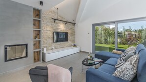 Een moderne woonkamer met een stenen muur, een flatscreen televisie, een bank en een eettafel met uitzicht op het buitengebied.