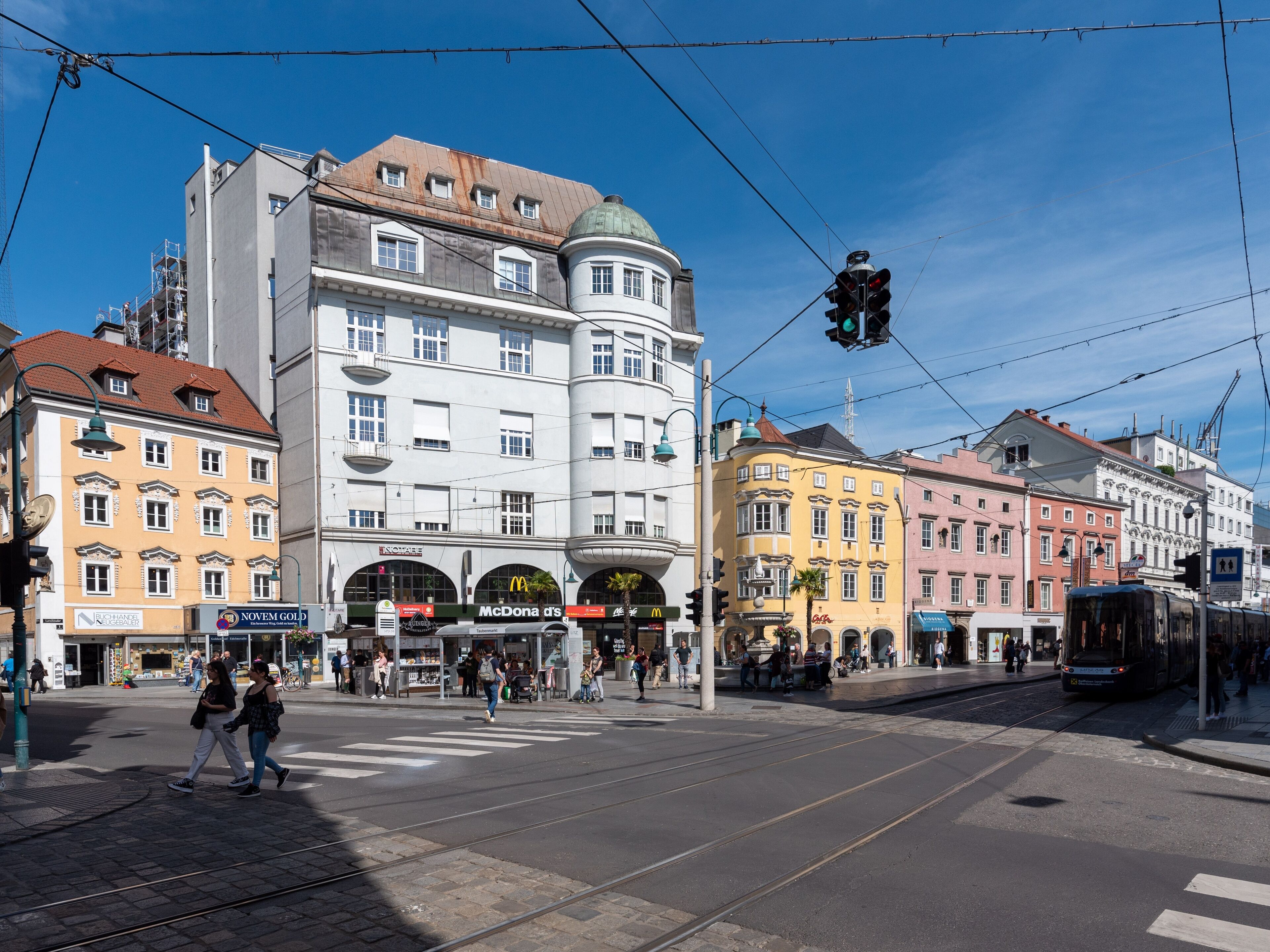 A street scene with tram tracks, buildings, and pedestrians.