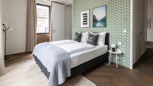 Un dormitorio con cama, mesita de noche, lámpara de pie y ventana con cortinas.