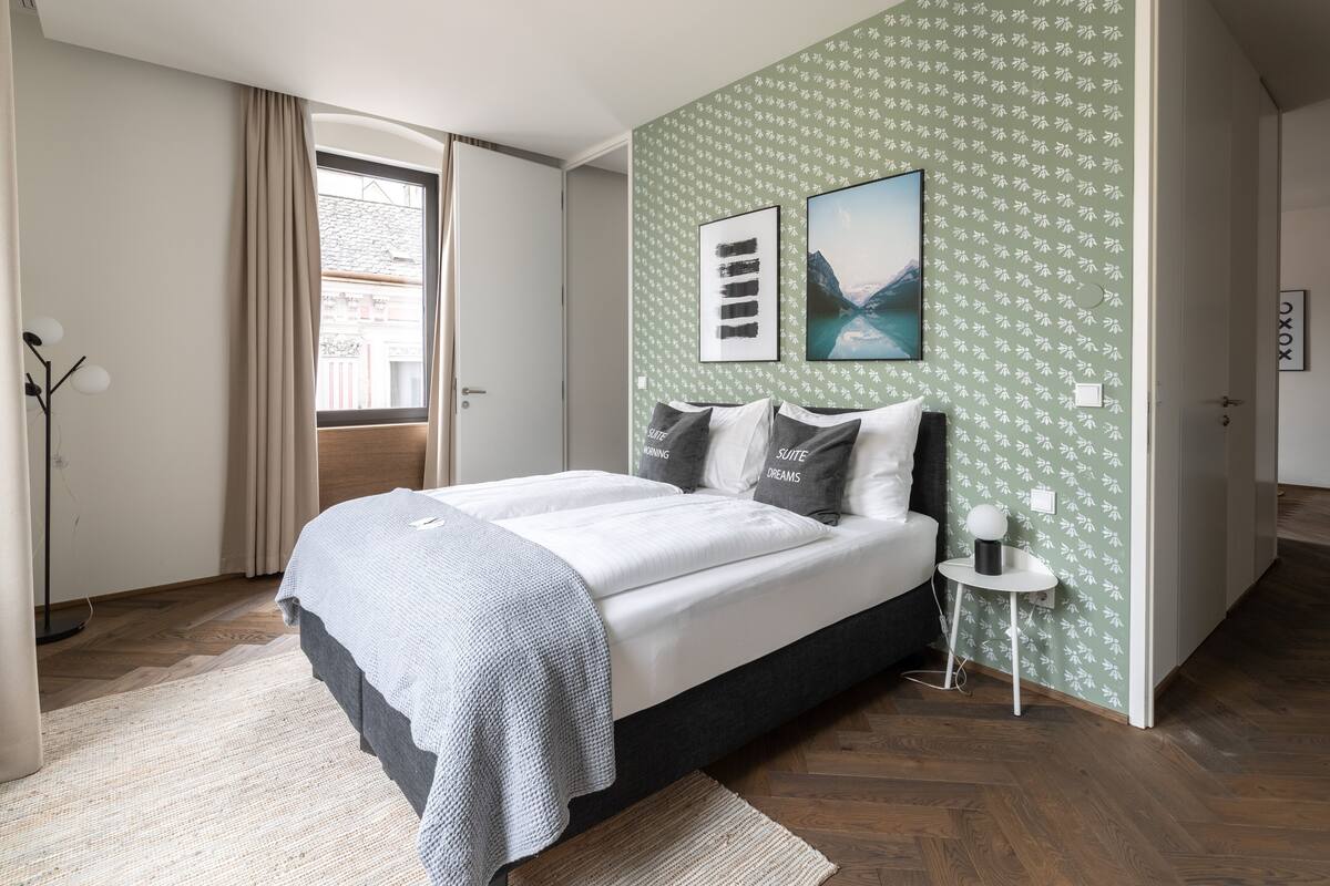 Ein Schlafzimmer mit Bett, Nachttisch, Stehlampe und einem Fenster mit Vorhängen.