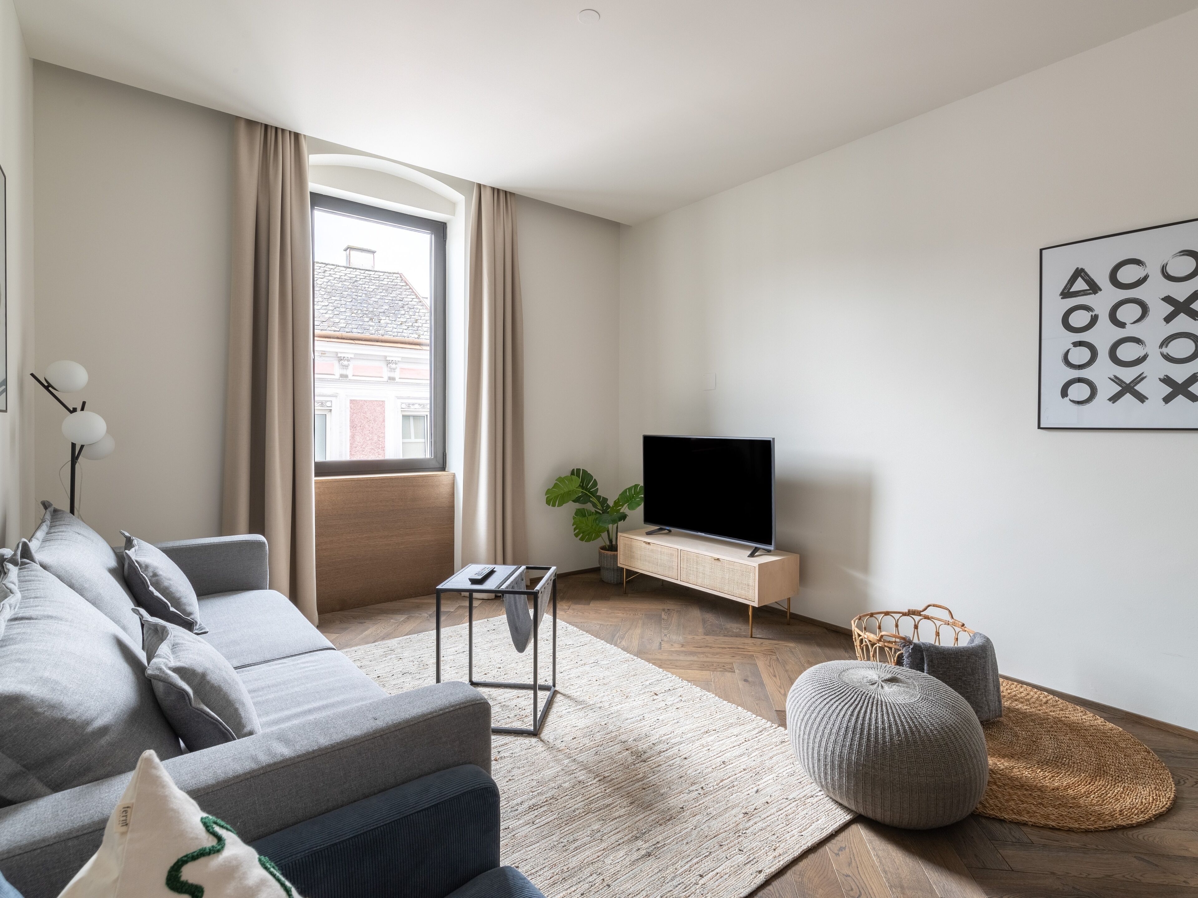 Un soggiorno moderno con un divano, una TV su un mobile in legno, un'ampia finestra con tende e un'opera d'arte a parete.