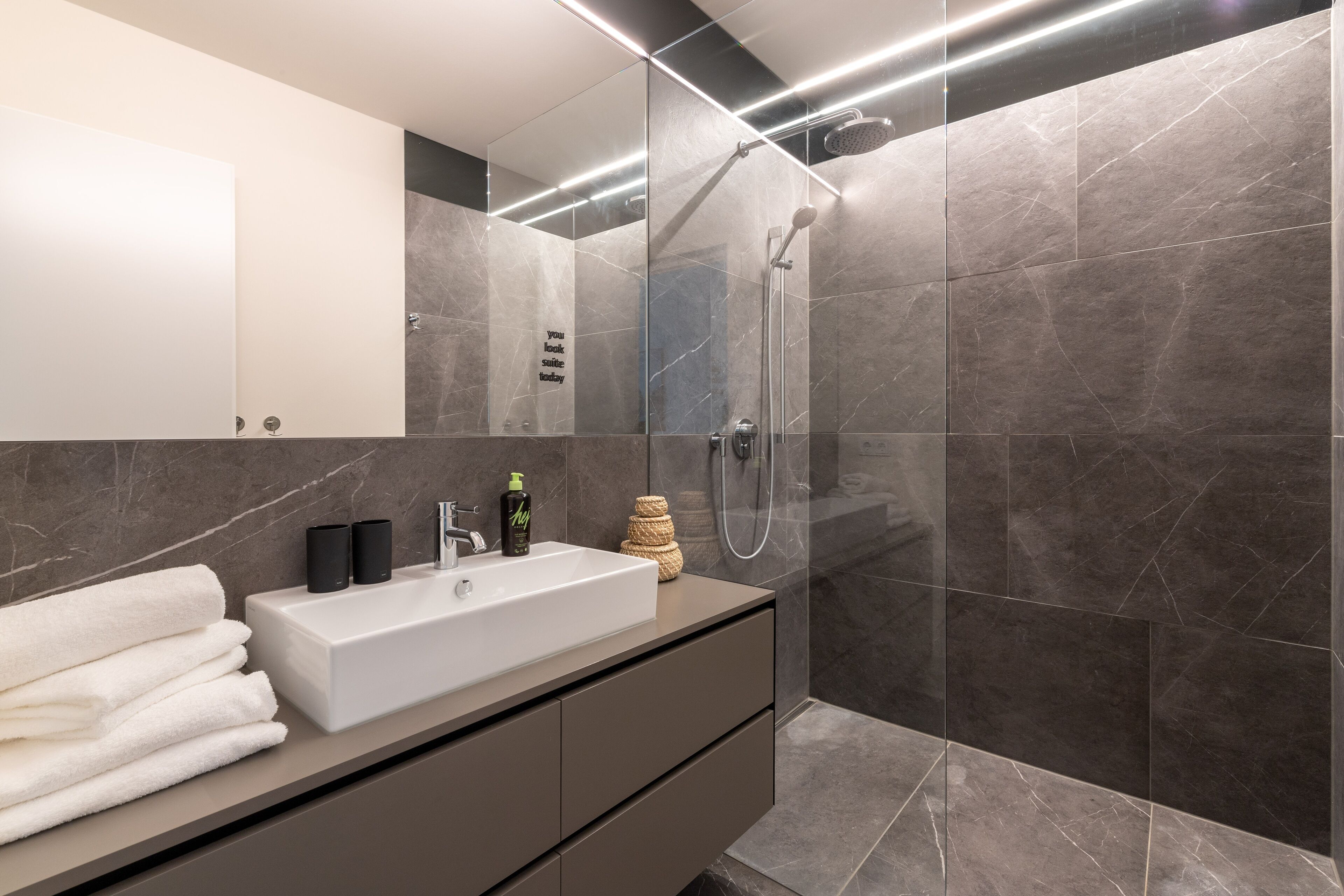 A modern bathroom with a large mirror, a white sink, and a glass-enclosed shower area.