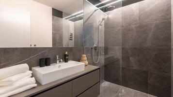 A modern bathroom with a large mirror, a white sink, and a glass-enclosed shower area.